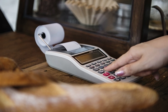 Ręka obsługująca przenośną kasę fiskalną na ladzie sklepowej.