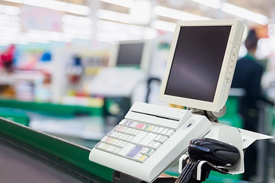 Stanowisko kasowe z monitorem i czytnikiem kodów w supermarkecie.