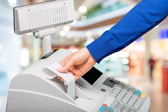 Ręka wyciągająca paragon z kasy fiskalnej w sklepie.