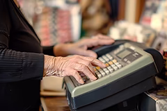 Starsza osoba obsługująca kasę fiskalną w sklepie.