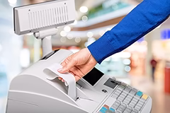 Ręka wyciągająca paragon z kasy fiskalnej w sklepie.